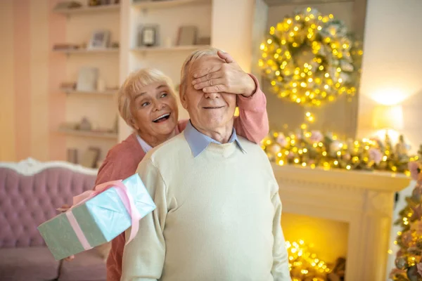 Äldre kvinna ger julklapp till sin man och blundar med handen — Stockfoto