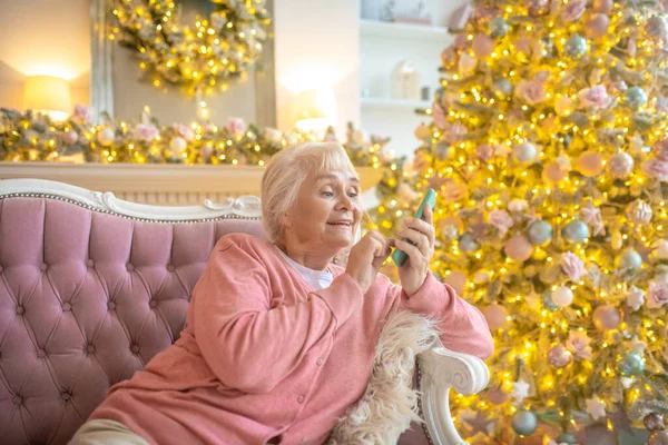 Starsza kobieta siedzi na kanapie i trzyma smartfona — Zdjęcie stockowe