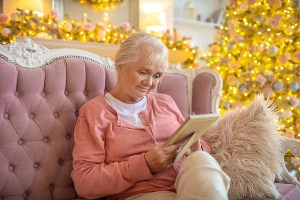 Starší žena sedící na pohovce s fotkou v ruce — Stock fotografie