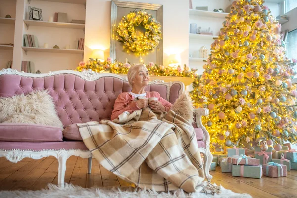 Femme âgée assise sur un canapé avec une tasse de thé et regardant réfléchi — Photo