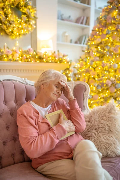 Senior kvinna sitter på en soffa med ett foto i handen och ser ensam — Stockfoto