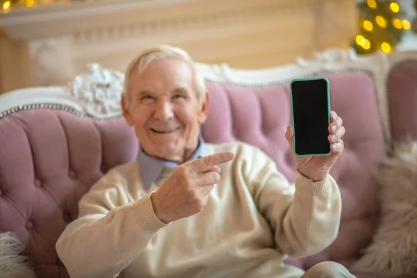 Γκρίζα μαλλιά άνθρωπος κάθεται σε έναν καναπέ με ένα smartphone στα χέρια και αναζητούν ικανοποιημένοι — Φωτογραφία Αρχείου