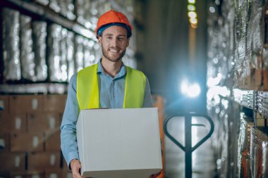 Genç erkek işçi bir kutu taşıyor ve gülümsüyor.