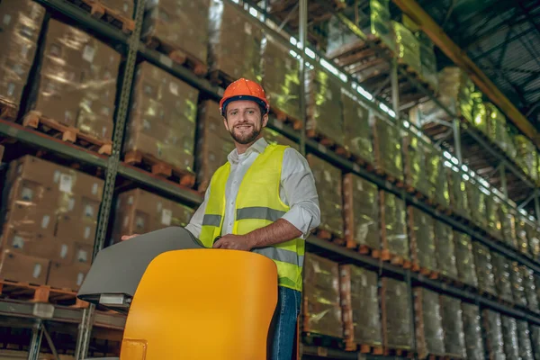 Armazém trabalhador em capacete laranja em pé perto de prateleiras com recipientes — Fotografia de Stock