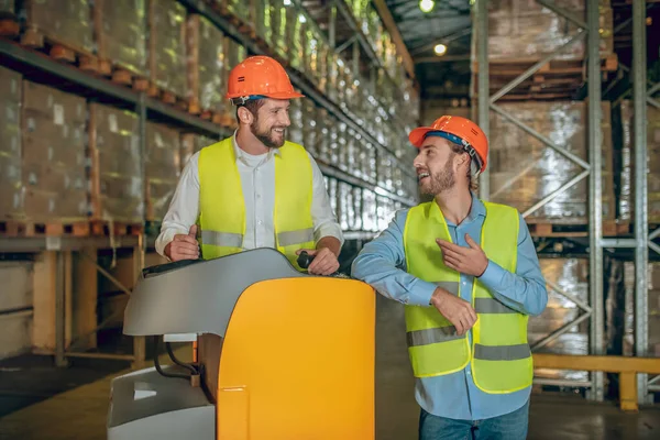 Travailleurs d'entrepôt dans des casques orange debout près des étagères et parlant — Photo