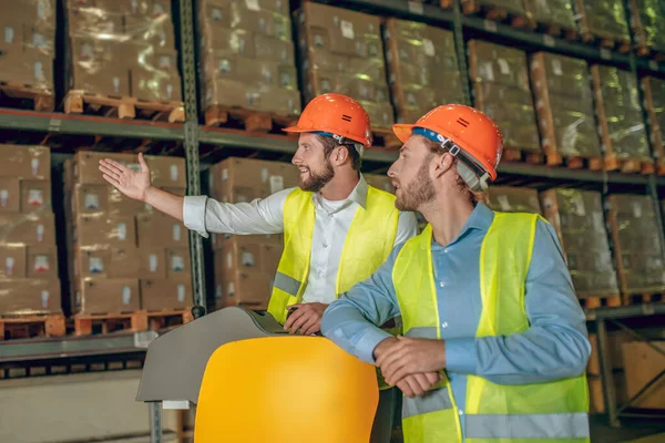 Pakhuismedewerker in oranje helm laat iets zien aan zijn collega — Stockfoto