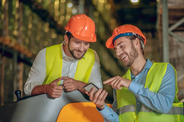 직장 동료에게 스마트폰으로 무엇인가를 보여 주면서 웃고 있는 수리공 직원 — 스톡 사진