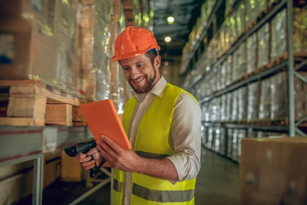 Trabalhador do armazém em colete amarelo olhando para o tablet e sorrindo — Fotografia de Stock