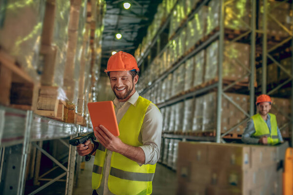 Warehouse worker in yellow vest holding a tablet in his hands