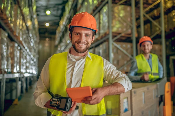 Twee magazijnmedewerkers in helmen die goederen controleren en er positief uitzien — Stockfoto