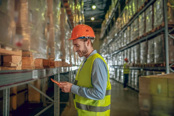 Männlicher Lagerarbeiter mit Helm steht in der Nähe von Containern und hält ein Tablet in der Hand — Stockfoto