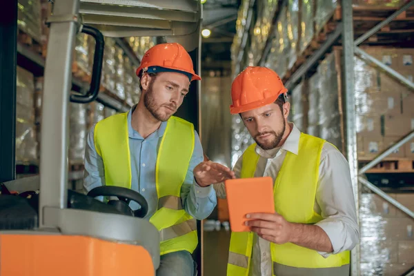 Dois trabalhadores de armazém em capacetes verificando informações on-line — Fotografia de Stock