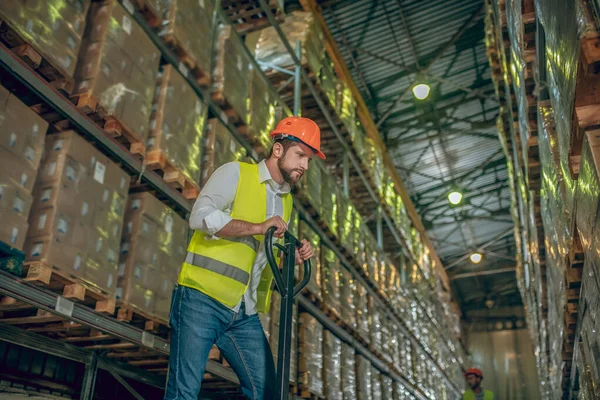 Trabalhador em um colete e capacete empurrando o carregador — Fotografia de Stock