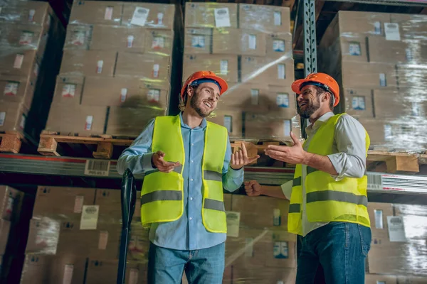 Dos trabajadores con chalecos amarillos discutiendo algo en el almacén — Foto de Stock