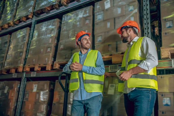 Dos trabajadores con chalecos amarillos hablando en el almacén — Foto de Stock