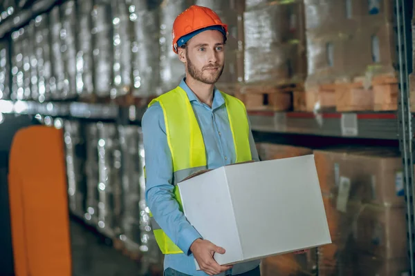 Jonge mannelijke werknemer die een doos draagt en er ernstig uitziet — Stockfoto