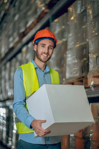 Joven trabajador masculino llevando una caja y luciendo positivo — Foto de Stock