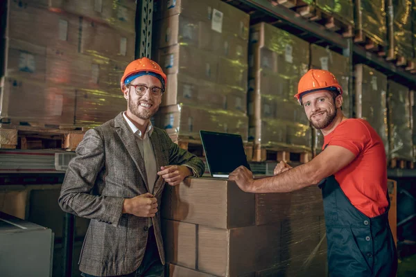 Pracovník a manažer skladu stojí v blízkosti kartonových krabic a vypadá pozitivně — Stock fotografie