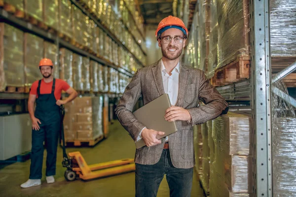 Warehouse manager in orange helmet holding a laptop — Stock Photo, Image