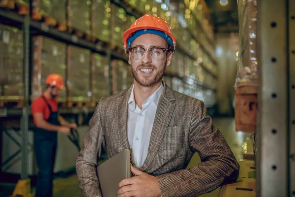 Magazijn manager in oranje helm met een laptop en een glimlach — Stockfoto