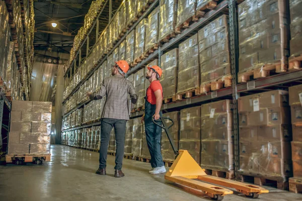 Manager talking to a warehouse worker and showing him containers — Stock Photo, Image