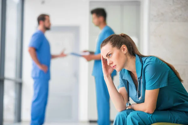 Молода жінка-лікар почувається засмученою, поки її колеги говорять — стокове фото