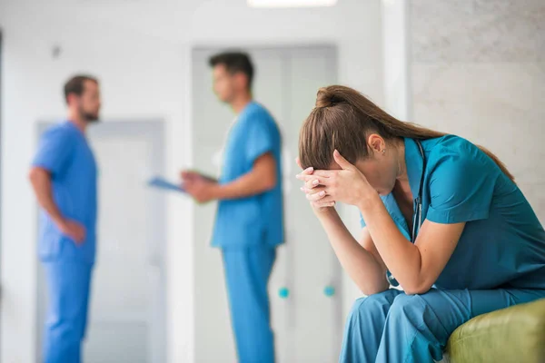 Jovem médica sentindo-se infeliz enquanto seus colegas conversam — Fotografia de Stock