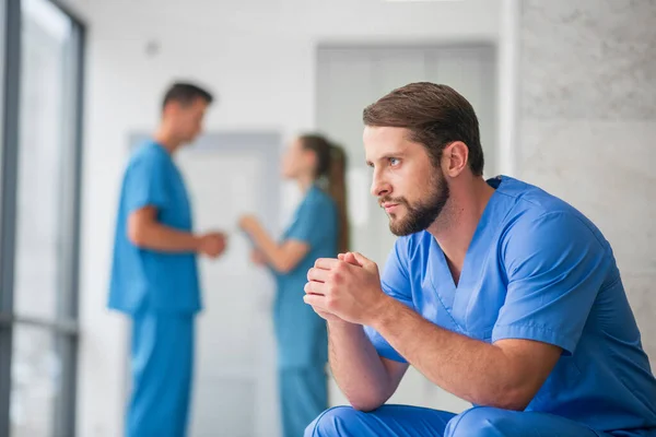 Jeune médecin masculin se sentant réfléchi pendant que ses collègues parlent — Photo