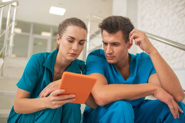 Dos trabajadores médicos sentados en las escaleras y mirando algo en la tableta —  Fotos de Stock