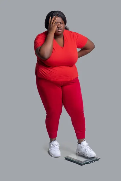 Ung mörkhyad kvinna i röda kläder kollar vikt och känner sig besviken — Stockfoto