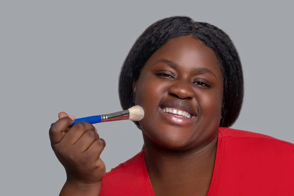 Молодая темнокожая женщина в красной одежде держит кисть для макияжа — стоковое фото