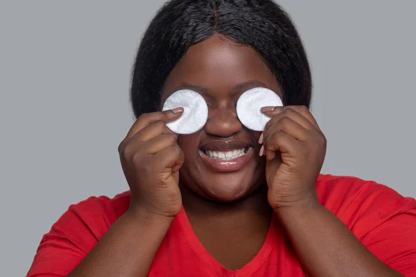 Młoda kobieta o ciemnej skórze trzyma gąbkę do oczyszczania twarzy i wygląda pozytywnie. — Zdjęcie stockowe