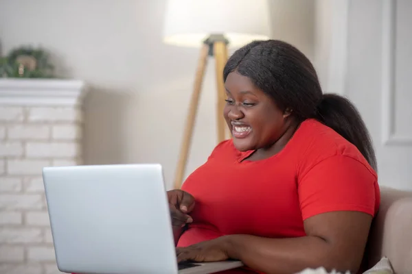 Femme afro-américaine assise dans sa chambre avec un ordinateur portable et l'air surpris — Photo