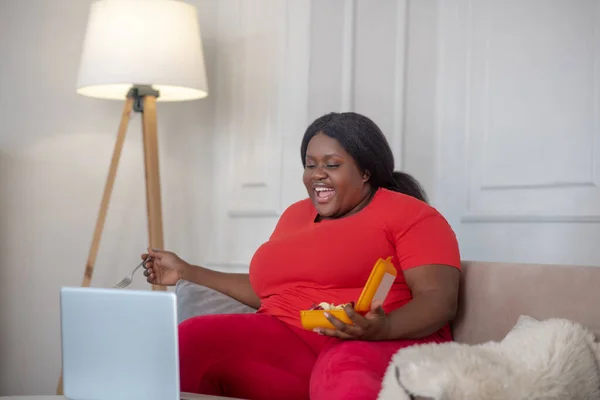 Plusz méretű afro-amerikai nő néz valamit, és eszik — Stock Fotó