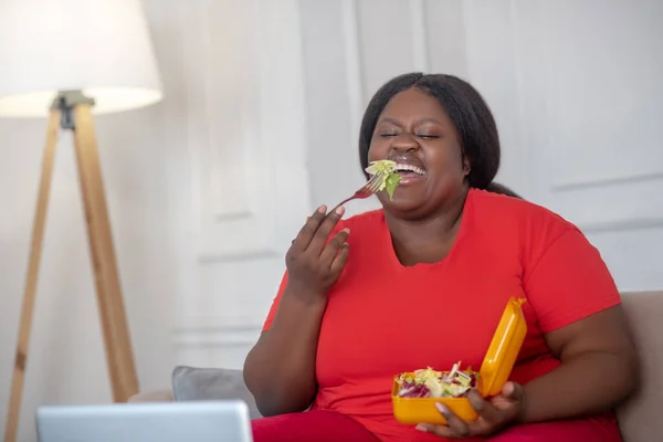 Plus size afrikanisch amerikanisch frau beobachten etwas und genießen ihr essen — Stockfoto