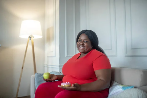 还有个头大的非洲裔美国女人，手里拿着苹果和甜甜圈，看上去有些犹豫 — 图库照片