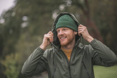 Yeşil ceketli genç adam yağmurda yürüyor.