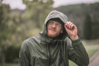 Kapüşonlu genç adam yağmuru izliyor.