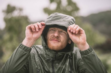 Yağmurun altında duran kapüşonlu genç sakallı adam