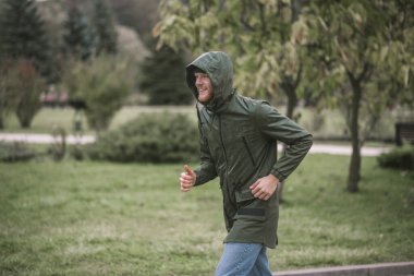 Yağmurun altında giden kapüşonlu genç sakallı adam.