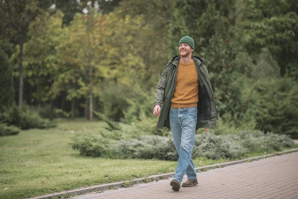 Jovem de casaco verde caminhando no parque — Fotografia de Stock