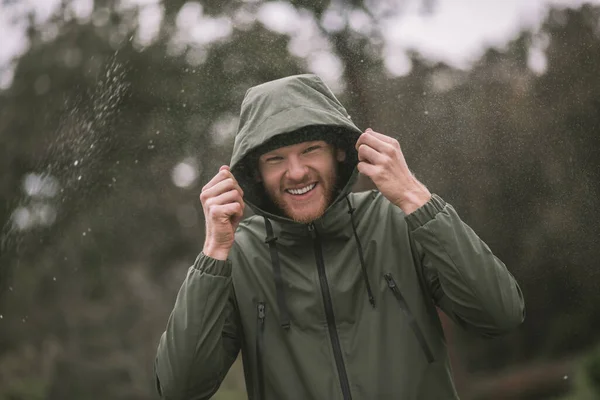Jovem com um casaco verde andando na chuva e sorrindo — Fotografia de Stock