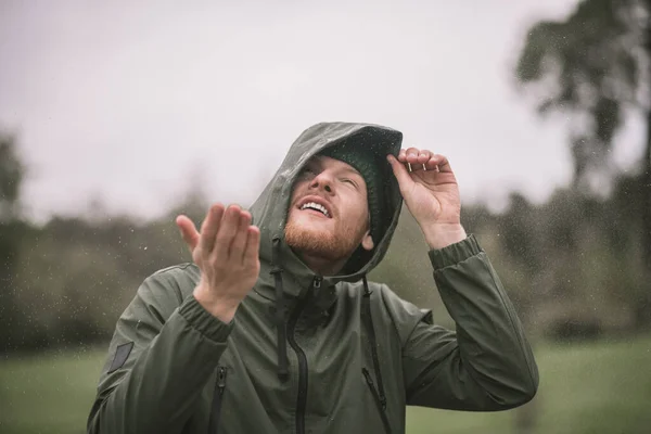 Young man in a green coat catching rain drops