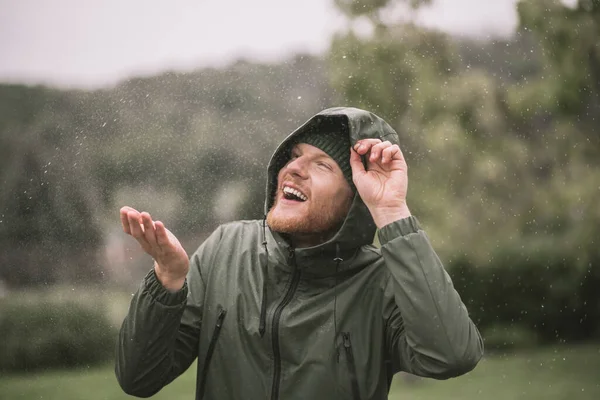 Young man in a green coat catching rain drops — Stock Photo, Image