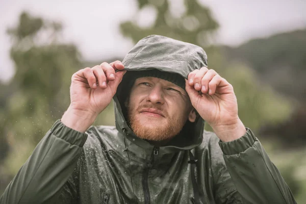 Yağmurun altında duran kapüşonlu genç sakallı adam — Stok fotoğraf