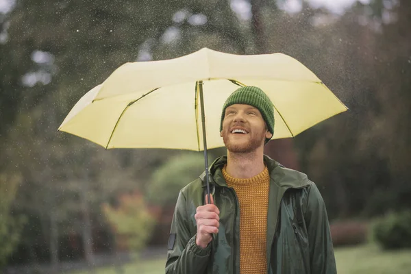 Young bearded man standing with yellow umbrella in hand — Stock Photo, Image