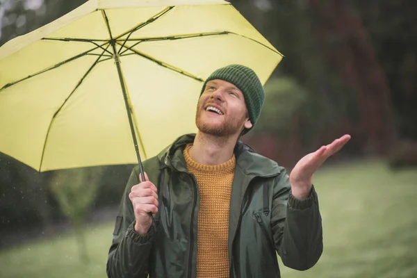 Young bearded man standing with yellow umbrella under the rain — Stock Photo, Image