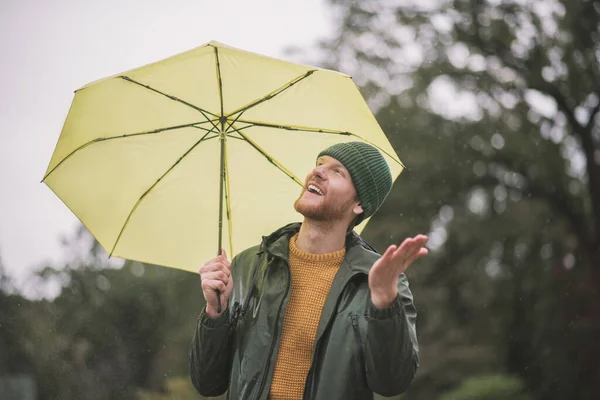 Young bearded man standing with yellow umbrella under the rain — Stock Photo, Image