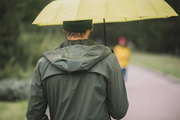 Young bearded man under yellow umbrella waiting for his girlfriend — Stock Photo, Image