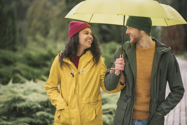 Молодая пара под желтым зонтиком выглядит счастливой — стоковое фото